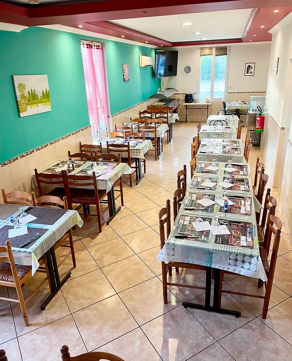 Ambiance chaleureuse dans notre salle de restaurant bistro Intérieur de restaurant décoré murs turquoise et rouge, chaises bois, et tables dressées. Un comptoir buffet est visible au fond.